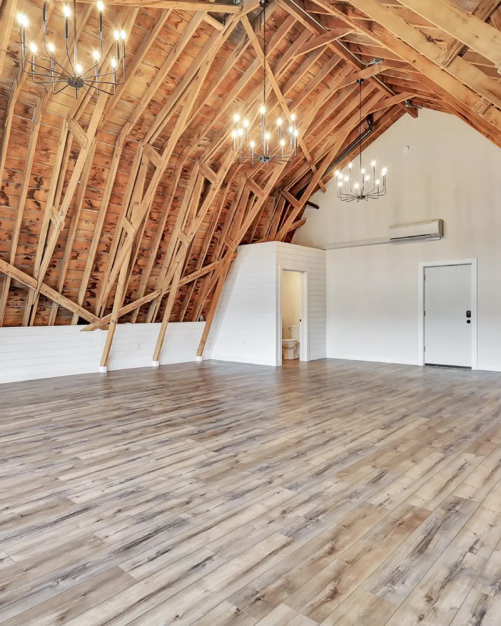 Spacious empty room with a high, curved wooden beam ceiling and large windows along one wall. Light wood flooring extends across the open space, giving it a bright, modern feel | Borealis Bison Barns | Palmer, AK