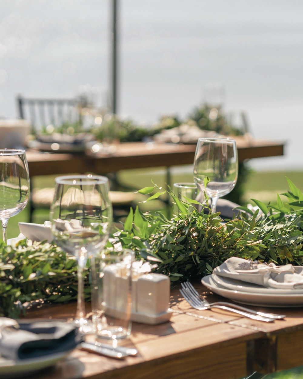Close-up of styled reception table with greenery centerpiece, plates, and glassware at Borealis Bison Barns