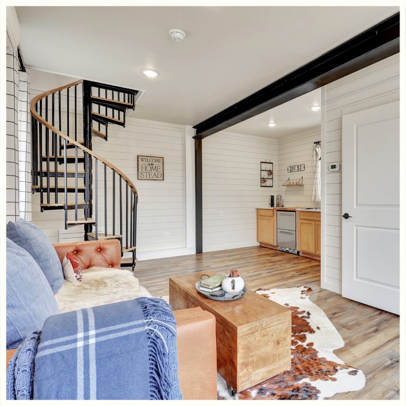Cozy interior with sofa, wood floors, spiral staircase, and small kitchenette, accented by a cowhide rug. Borealis Bison Barns | Palmer, AK