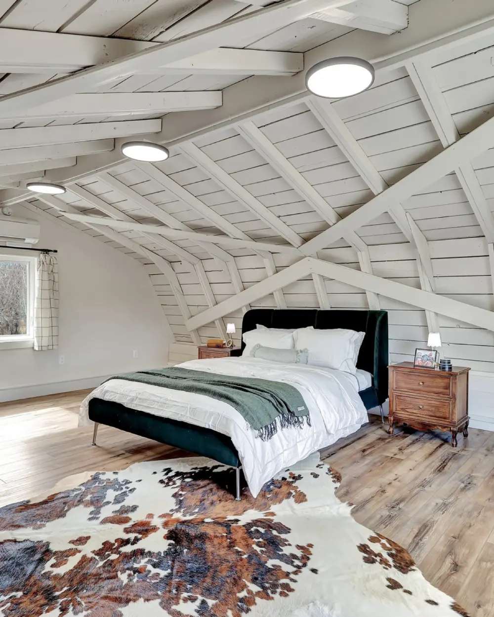Bedroom with a curved white wood-beam ceiling, large bed, nightstands, and cowhide rug on wood flooring. Borealis Bison Barns | Palmer, AK