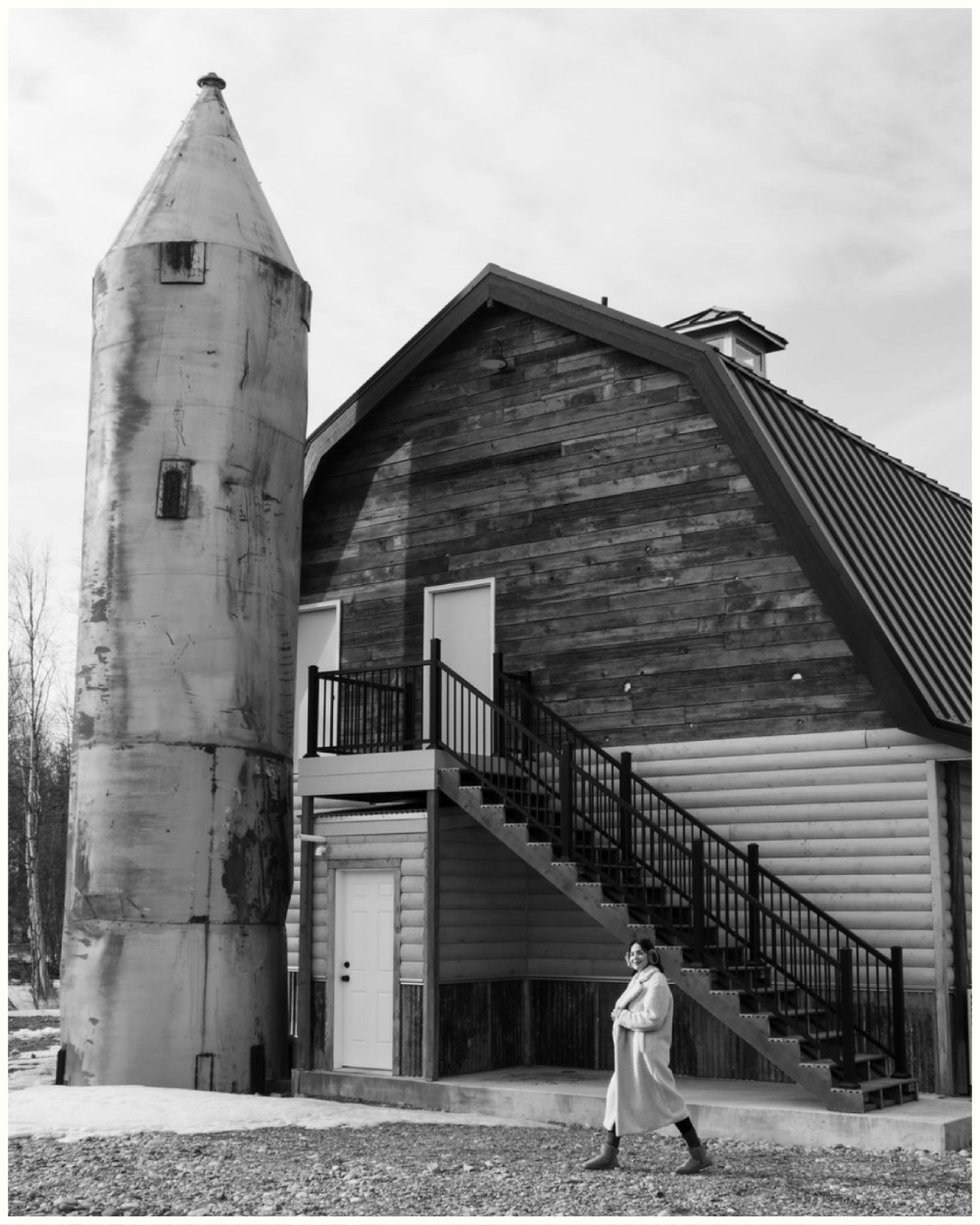 Woman walking beside rustic barn and silo at Borealis Bison Barns in Palmer Alaska