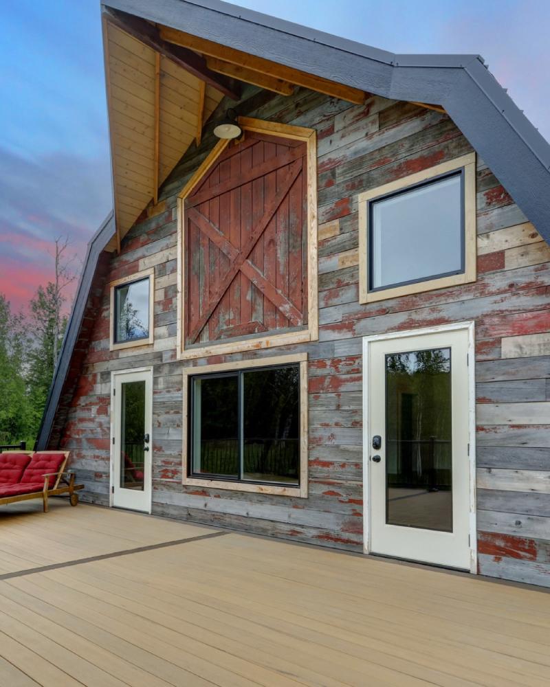 Wraparound deck at Borealis Bison Barns featuring restored barn wood siding, historic barn doors, and spacious outdoor gathering space in Alaska.
