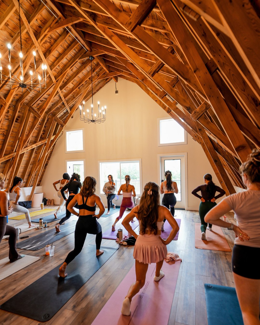 Group fitness class beneath exposed wood beams and chandeliers inside Borealis Bison Barns.